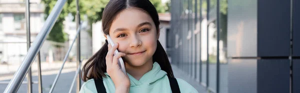 Lächelndes Schulkind, das auf dem Smartphone spricht und auf der Straße in die Kamera schaut, Banner — Stockfoto