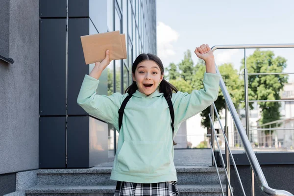 Aufgeregtes Schulkind hält Bücher in der Hand und blickt in die Kamera auf der Straße — Stockfoto
