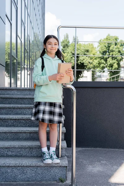 Веселий школяр тримає книги, стоячи на сходах на міській вулиці — стокове фото