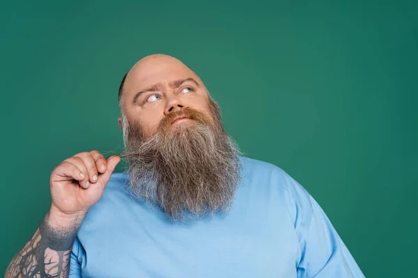 Thoughtful man with overweight touching beard and looking away isolated on green — Stockfoto