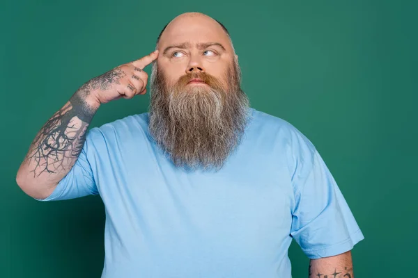 Tatuato plus size uomo toccare la testa e guardando altrove, mentre il pensiero isolato sul verde — Foto stock