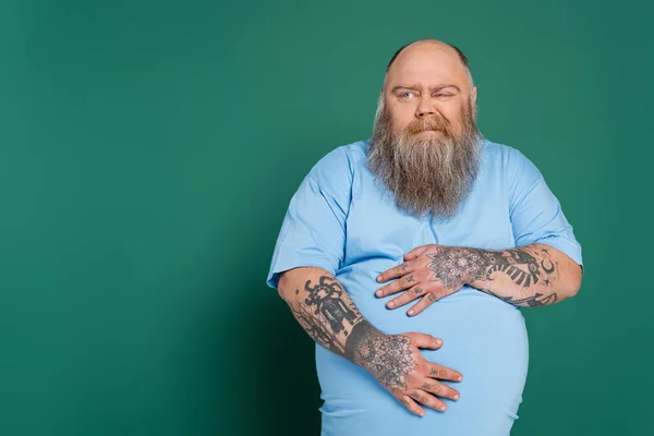 Displeased overweight man hugging tummy while suffering from stomach pain isolated on green — Photo de stock
