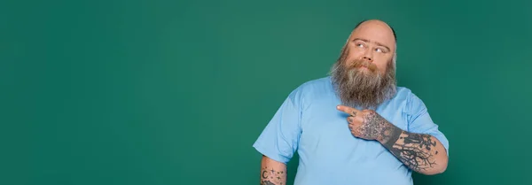 Thoughtful overweight man with beard looking away and pointing with finger isolated on green, banner — Foto stock