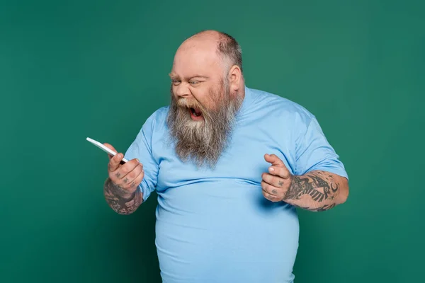 Irritated overweight man shouting while sending voice message on smartphone isolated on green — Stockfoto