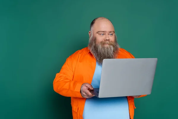 Bearded positive man with overweight looking at laptop isolated on green — Photo de stock