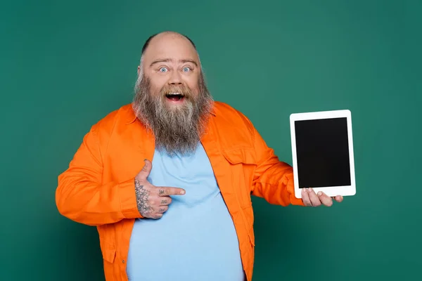 Amazed overweight man pointing at digital tablet isolated on green — Stockfoto