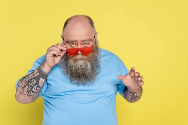 Hombre serio más tamaño mirando a la cámara sobre gafas de sol de moda aislado en amarillo - foto de stock