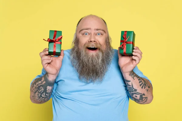 Astonished overweight man with tattoos showing presents isolated on yellow — Photo de stock