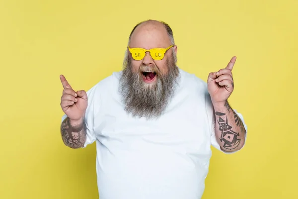 Bold and bearded overweight man in glasses with sale lettering pointing with fingers isolated on yellow — Stock Photo