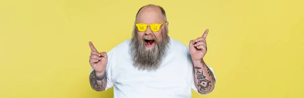 Asombrado hombre con sobrepeso en gafas con letras de venta apuntando con los dedos aislados en amarillo, bandera - foto de stock