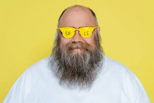 Smiling plus size man with beard wearing glasses with sale lettering isolated on yellow — Photo de stock