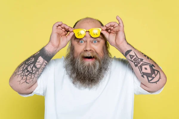 Étonné tatoué plus taille homme tenant des lunettes avec vente lettrage isolé sur jaune — Photo de stock