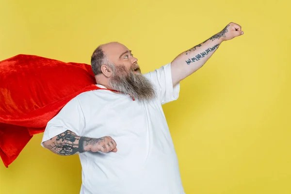 Screaming overweight man posing in superhero cloak with outstretched hand isolated on yellow — Stock Photo