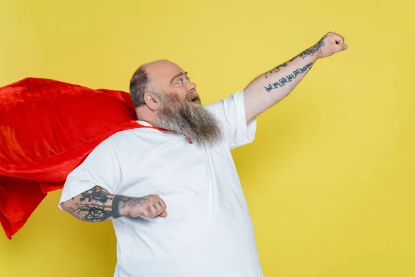 Hurlant homme en surpoids posant en manteau de super-héros avec la main tendue isolé sur jaune — Photo de stock