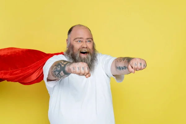 Homem com sobrepeso barbudo em traje de super-herói gritando com as mãos estendidas isoladas no amarelo — Fotografia de Stock