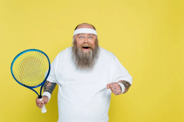 Sorprendido y alegre jugador de tenis con sobrepeso mirando la cámara aislada en amarillo - foto de stock