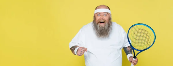 Excited overweight man with tennis racquet looking at camera isolated on yellow, banner — Stock Photo