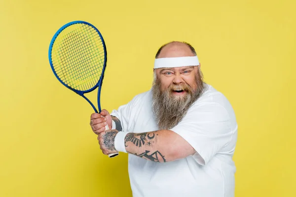 Thrilled overweight and tattooed man playing tennis isolated on yellow — Photo de stock