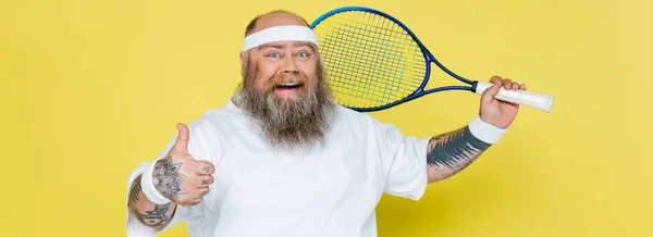 Cheerful plus size tennis player showing thumb up isolated on yellow, banner — Stock Photo