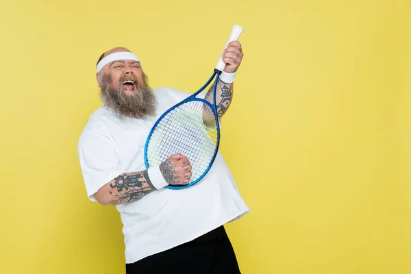 Allegro plus size uomo divertirsi con racchetta da tennis isolato su giallo — Foto stock