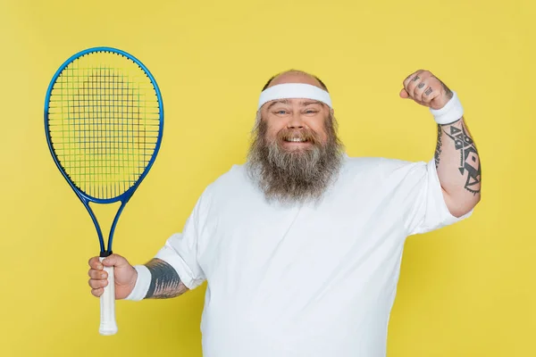 Happy and overweight tennis player showing win gesture and looking at camera isolated on yellow — Stockfoto