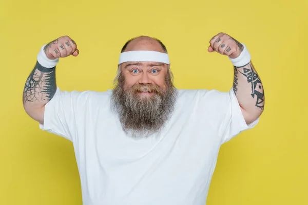 Татуйований спортсмен з надмірною вагою демонструє силу ізольовану на жовтому — стокове фото