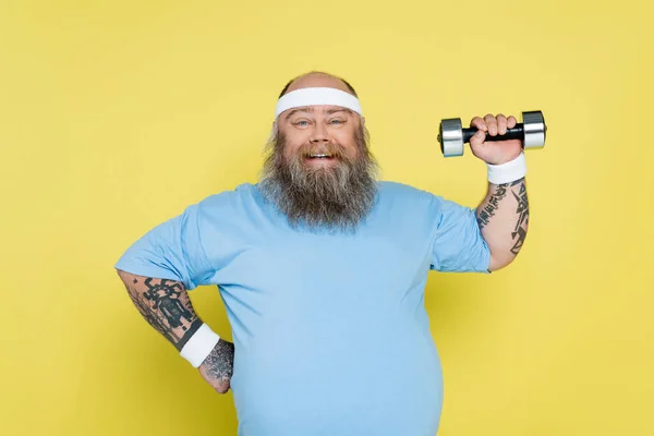 Happy overweight man standing with hand on waist and training with dumbbell isolated on yellow — Photo de stock