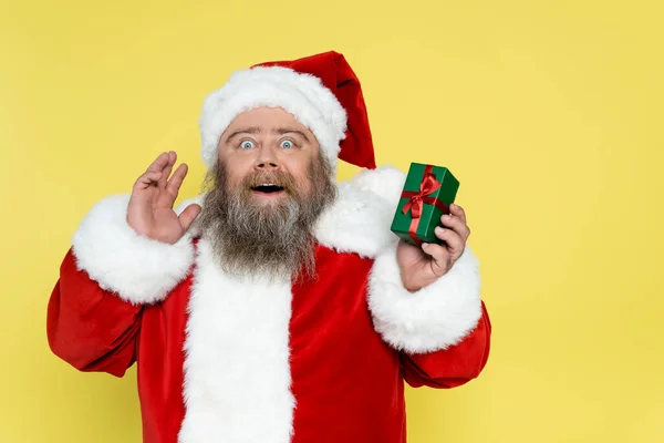 Amazed plus size man in christmas costume holding present isolated on yellow — Foto stock