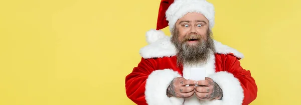 Thrilled plus size man in christmas costume messaging on mobile phone isolated on yellow, banner — Foto stock
