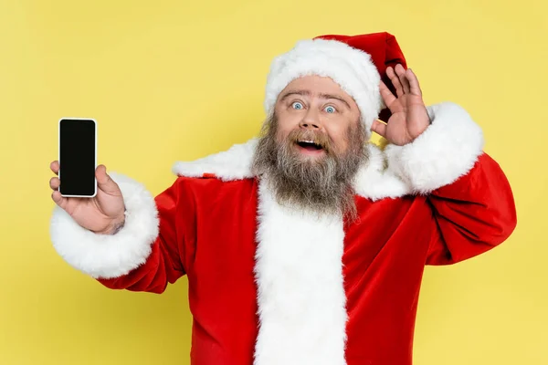 Étonné et potelé santa claus montrant smartphone avec écran vide isolé sur jaune — Photo de stock