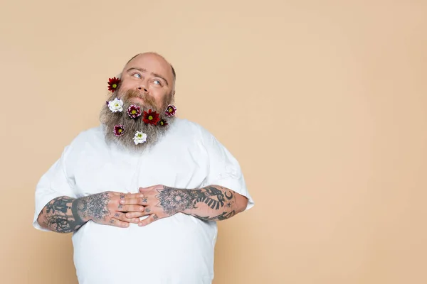 Heureux homme en surpoids avec des fleurs dans la barbe et les mains sur le ventre isolé sur beige — Photo de stock