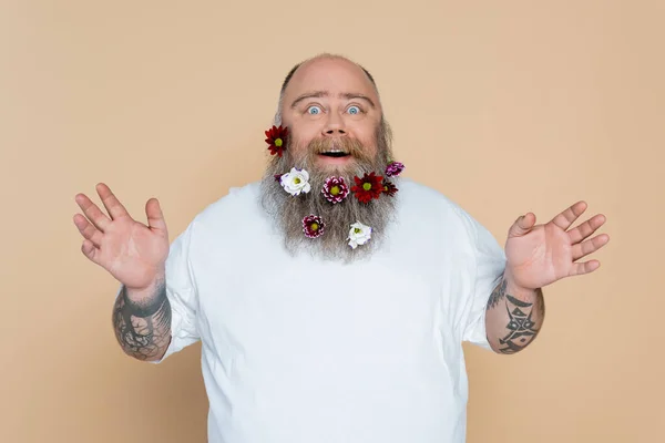 Homme en surpoids étonné avec des fleurs dans la barbe montrant wow geste isolé sur beige — Photo de stock