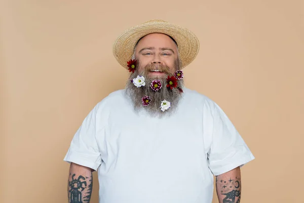 Uomo sovrappeso con barba decorata e cappello di paglia sorridente alla macchina fotografica isolata sul beige — Foto stock