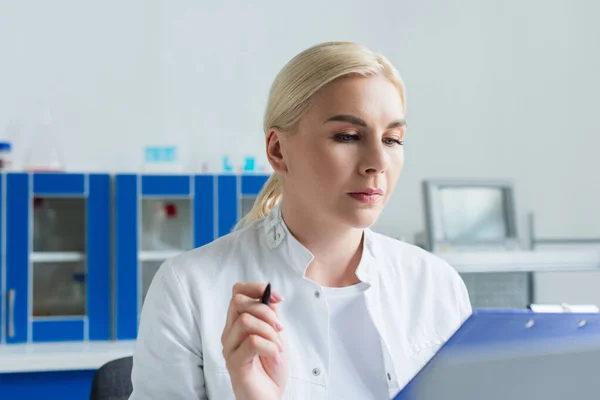 Scientist in white coat holding blurred clipboard in lab — Fotografia de Stock