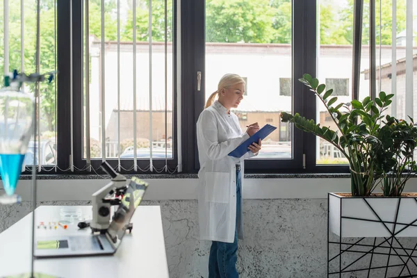 Side view of scientist writing on clipboard near window in laboratory — Foto stock