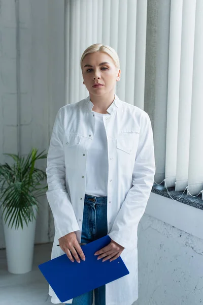 Blonde scientist holding clipboard and looking at camera in laboratory - foto de stock