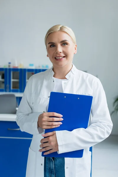 Cientista sorridente segurando prancheta e olhando para a câmera no laboratório — Fotografia de Stock