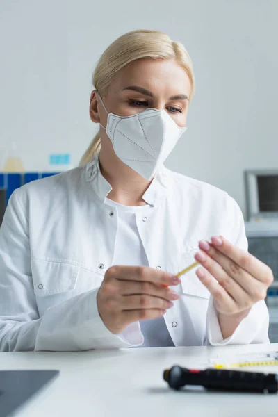 Blonde scientist in protective mask holding syringe in lab — стоковое фото