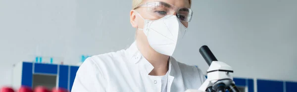Вчений в захисній масці дивиться на мікроскоп в лабораторії, банер — стокове фото