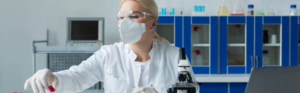 Scientist in protective mask holding test tube near microscope in laboratory, banner — Stockfoto