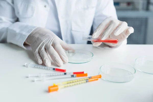 Cropped view of scientist in latex gloves holding test tube near petri dishes and syringes in lab — Photo de stock