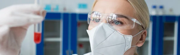 Scientist in protective mask holding blurred test tube in laboratory, banner — Stockfoto