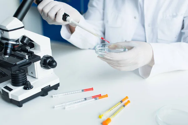 Cropped view of scientist working with electronic pipette and petri dish near microscope in lab — Stock Photo