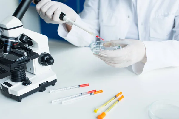 Cropped view of scientist working with electronic pipette and petri dish near microscope in lab — стоковое фото