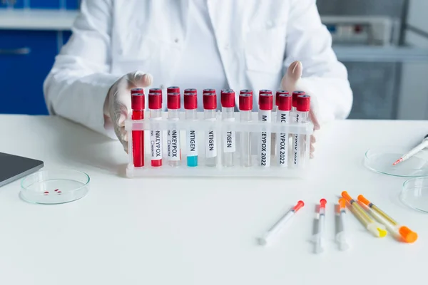 Cropped view of scientist holding test tubes with monkeypox lettering near syringes in lab — Stock Photo