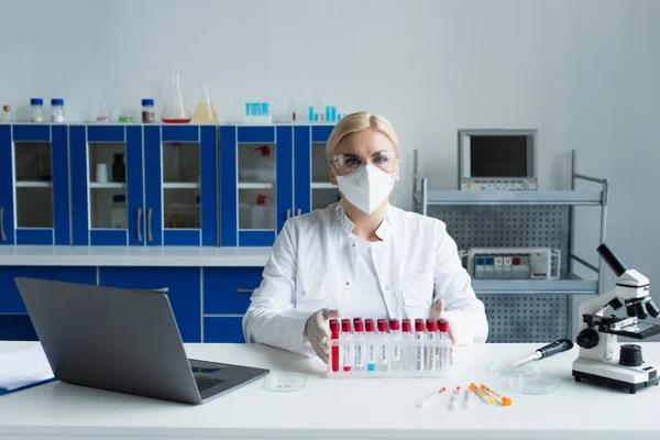 Scientist in protective mask looking at camera near test tubes and microscope in lab — Photo de stock