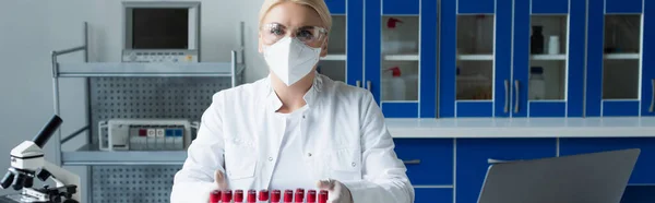 Scientist in goggles looking at camera near test tubes and microscope in lab, banner — Stockfoto