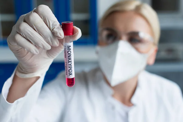 Blurred scientist in latex glove holding test tube with monkeypox lettering in laboratory — Stock Photo