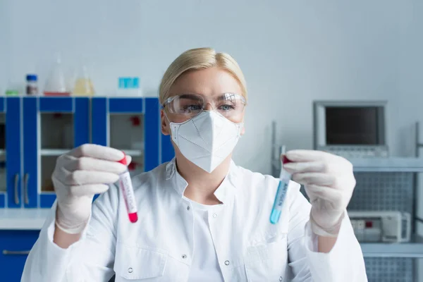 Wissenschaftler mit Schutzmaske hält verschwommene Reagenzgläser im Labor — Stockfoto