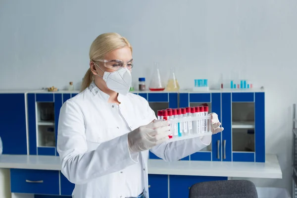 Cientista em luvas de látex e máscara protetora segurando tubos de ensaio em laboratório — Fotografia de Stock